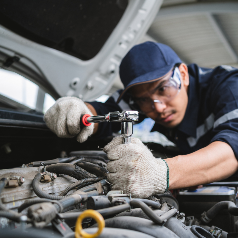 uniformed student under the hood making an adjustment to a vehicle engine