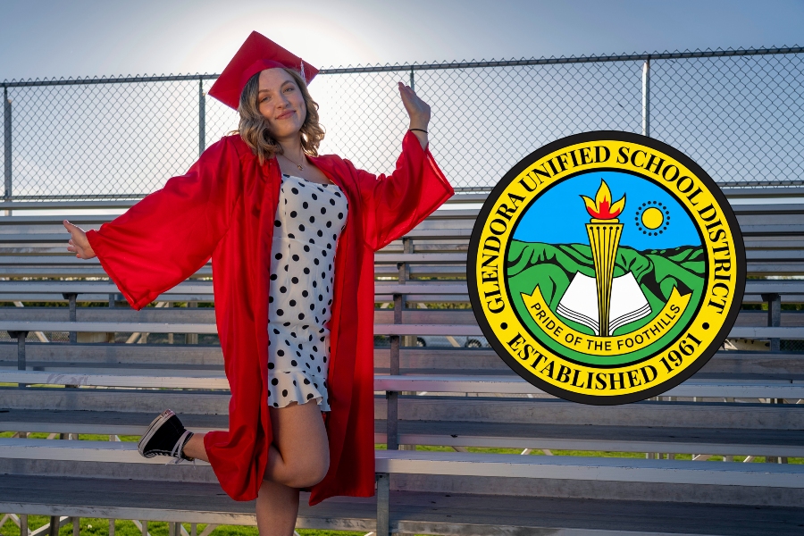 graduate in a red cap and gown poses on stadium bleachers beside the glendora unified school district seal