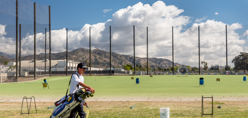 iconic shot of The Range at Citrus, facing east with a student golfer in the foreground and the San Gabriel Mountains and fluffy cumulus clouds in the background