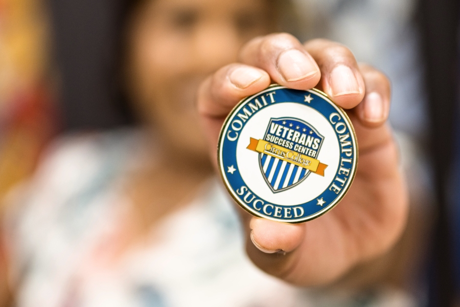 maria buffo, veterans success center director, holds a medallion toward the camera featuring the citrus college vsc logo in the center and the words - commit • complete • succeed - around the outer edge